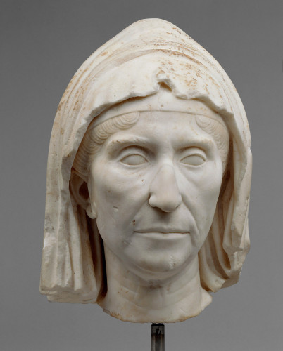 Description from the museum: “The old woman is wearing a mantle pulled across her head. Beneath the mantle a visible hair-band lies tight across her forehead. Hair-bands were also worn by priestesses, and the portrait’s subject may have performed this function in a cult. Covering the head was regarded as a gesture of chastity (Latin: castitas).
The portrait shows clear signs that the woman has aged, but they are not pronounced and underscore the high esteem and dignity of the elderly in the society of the Late Republic, familiar to us from numerous tomb portraits. The simple hairstyle is a development of a late-Hellenistic ideal and was in fashion for only a short time. This provides an important clue in dating the portrait to the time after the assassination of Caesar in 44 BC.”