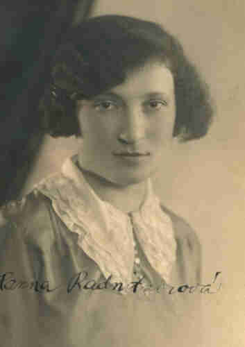 Portrait photograph of a young woman. The woman is looking centrally into the lens. She has a neutral expression on her face. She has slightly wavy dark hair pinned up on one side with a bobby pin at eye level. She is wearing a blouse with a white, decorated lace collar. 