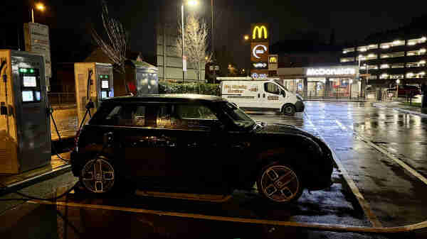 A black Mini parked at, and plugged into a charger, with a McDonald’s restaurant in the background 