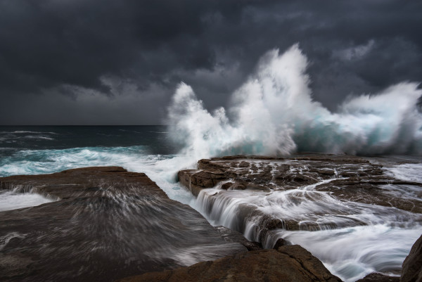 dark seascape during the storm with a big wave crashing against a rock platform