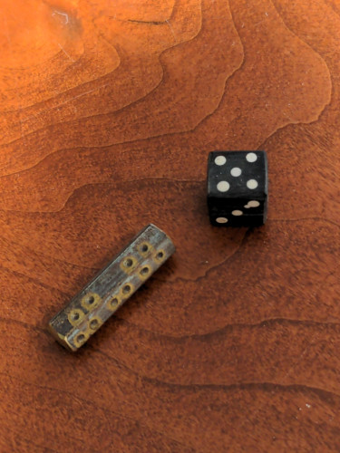 two dice:

on the left is a metal cylinder with hexagonal sides. on each side are small holes carved to create the normal die pips.

on the right is a normal d6, except it's been stained black with cream colored dots on each side. close inspection shows the carving grain of the bone used.