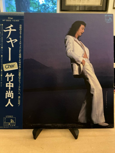 Record sleeve on a stand. A photograph of a man in a white jacket and pants but no shirt, leaning back against the background of Mt. Fuji at dusk.

A blue obi on the side reads "Char" and "Takenaka Hisato" (Char's real name) with the See•Saw logo at the bottom.