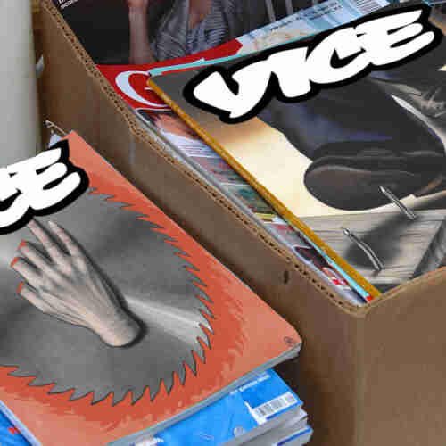 Piles of magazines in boxes. The top two magazines' covers have been replaced with faked up Vice covers. On one, a man's shoe is about to be punctured by a nail sticking up out of a board left on the ground. On the other, a rotary saw blade has amputated several fingers from someone's hand.
