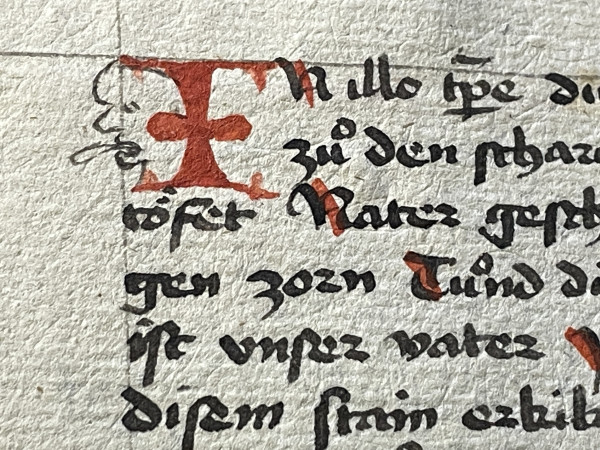 A red-ink initial "I" with knobs in its middle to make it fancy; to the right the text "In illo tempore" (with those standard Latin abbreviations) and below that the bits of german translation that was why this lectionary was copied -- so the nuns could understand and think on the readings of the day.

Within the left-hand side of the initial, someone has drawn a head in profile, with a rather bulbous nose. The fellow's mouth is open and something akin to a too-small speech bubble is coming out of his mouth