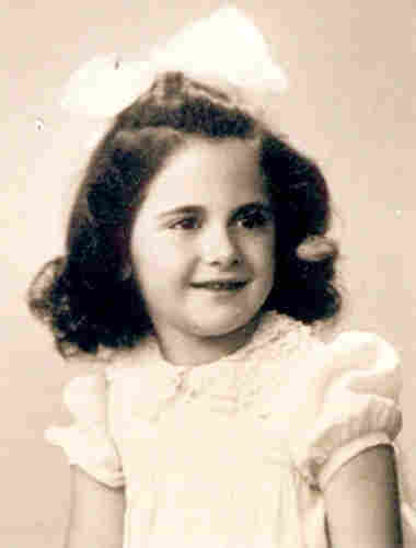 Portrait photograph of a girl of several years. She is wearing a short-sleeved blouse. She is wearing a large white bow in her dark hair.
