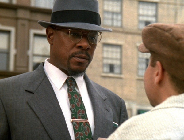 Benny Russell (played by Avery Brooks) is in a smart gray suit, gray hat, and glasses while he looks at a newspaper vendor played by Aron Eisenberg.