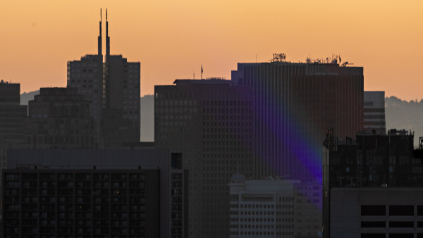 Sunrise behind the San Francisco skyline with a rainbow faintly exiting the urban canyon 