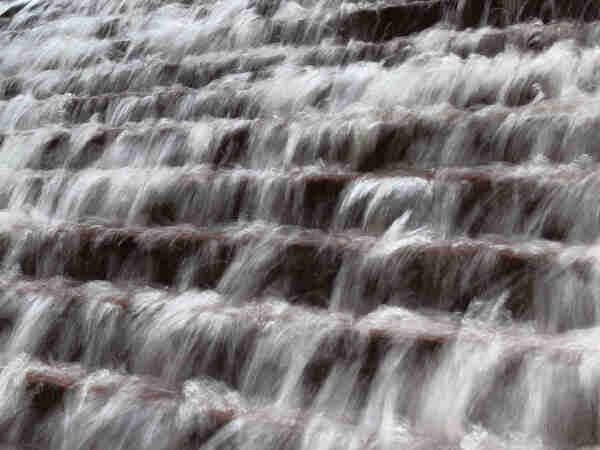 An abstract photo of water cascading down a stepped, waterfall-style  fountain. A slow shutter speed blurs the water.