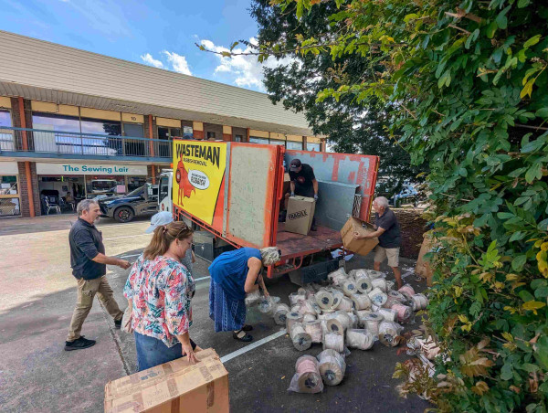 A photo of people picking up rolls of trims tipped from the back of a tilt truck onto the ground.