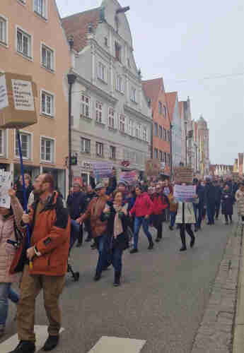 A group of people marching on a street of Donauwörth with protest signs against far right and nazis, with colorful buildings in the background.