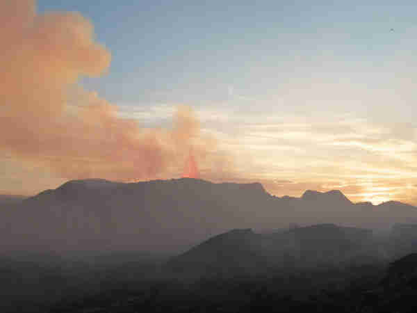 Le cratère de Litli-Hrutur en activité. On aperçoit vers la droite une projection de lave qui forme une pointe. L'endroit est envahi d'une fumée qui émane du cratère (dioxyde de soufre). Tout à droite le soleil est en train de se coucher.