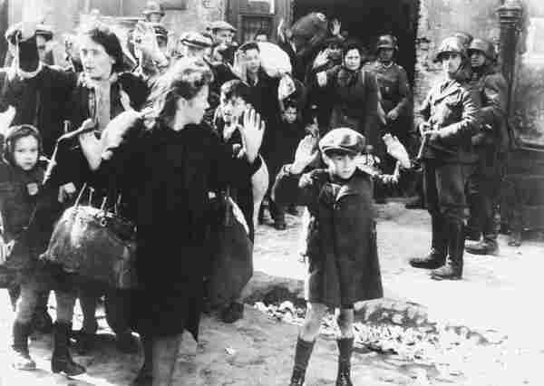 Jewish women and children forcibly removed from a bunker by Schutzstaffel (SS) units for deportation either to Majdanek or Treblinka extermination camps (1943). The are walking with their hands in the air, with Nazi soldiers aiming guns at them. By Unknown author (Franz Konrad confessed to taking some of the photographs, the rest was probably taken by photographers from Propaganda Kompanie nr 689.[1][2]) - Image:Warsaw-Ghetto-Josef-Bloesche-HRedit.jpg uploaded by United States Holocaust MuseumThis is a retouched picture, which means that it has been digitally altered from its original version. Modifications: Restored version of Image:Stroop Report - Warsaw Ghetto Uprising 06.jpg with artifacts and scratches removed, levels adjusted, and image sharpened.., Public Domain, https://commons.wikimedia.org/w/index.php?curid=17223940