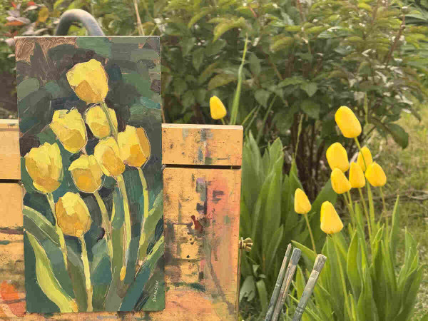 a photo of a cluster of yellow tulips. there is an artist easel on the left with an oil painting of the tulips.  i think the artist did a good job!