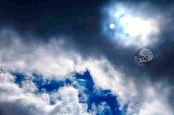dark clouds and patches of blue sky illuminated brightly by the sun, which is visible through the haze of clouds