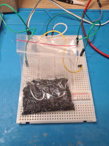 A bag of tiny ferrite cores (about 32 thousand cores in the bag, if I am to believe the labeling)  in a zip lock on top of a bread board