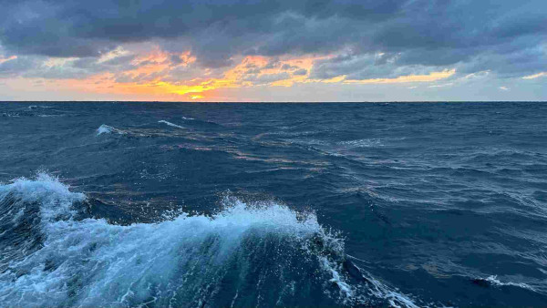 Sunset at sea with a wave in the foreground. 