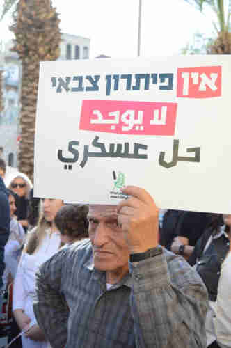 A person holding a sign above their head that reads “There Is No Military Solution” in Hebrew and Arabic.