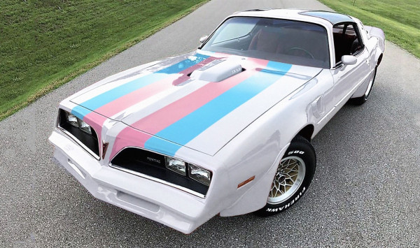 A picture of a white 70s pontiac trans am with pink and blue stripes up the hood in trans flag colours. Trans Am. Trans Trans Am.