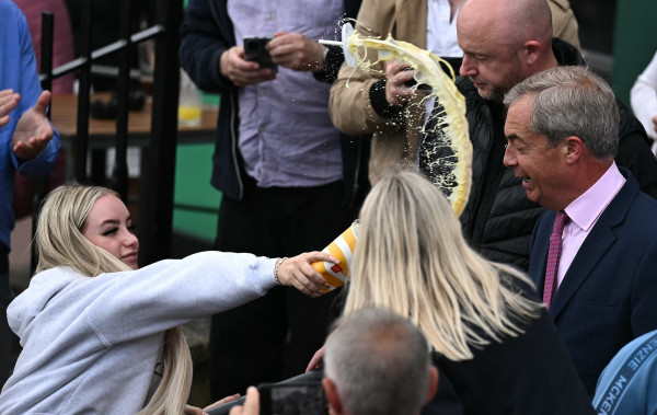 A photo of a young woman throwing a milkshake at Nigel Farage. The shot has caught the incident just before impact and the stream of milkshake just inches away from Farage's face.