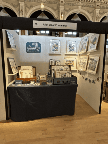 Our stand at Craft Festival Cheltenham with framed prints on the walls and a fabric covered table at the front. 