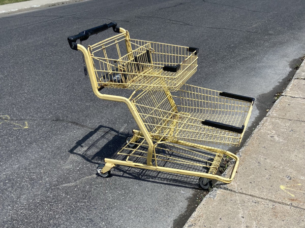 An abandoned yellow grocery cart on an asphalt street, pushed up against the concrete curb. 