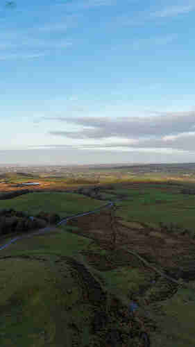 Aerial shot over moorland and farmland with clear blue skies and whispy clouds