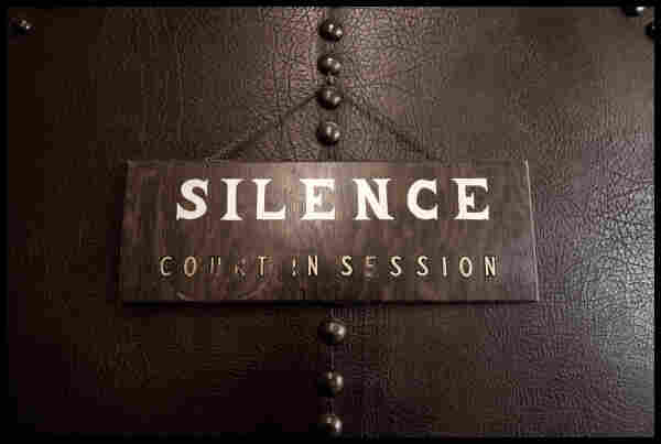 A well-worn wooden sign with stencilled white letters hangs on a leather-clad panel. The sign reads:

SILENCE

COURT IN SESSION