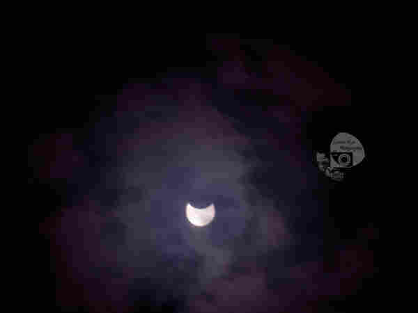 a purple hued shot of a partial solar eclipse against a dark background.