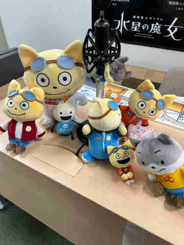 A group of space-themed soft plushies, most of them cats wearing googles, are clustered around a mic. The cat character is named “Kotetsu” and is from a TV anime. 