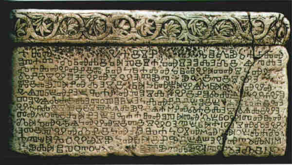 The Baška tablet. It is a yellowing stone tablet with a round decoration of leaves on a raised section at the top, and a lot of letters in the glagolitic script beneath. A large crack runs up the right hand side.