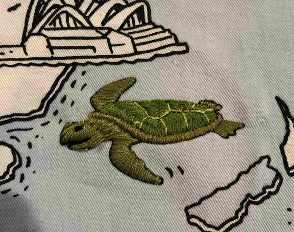 An embroidered turtle. Its various shades of green and looks happy 