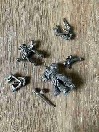 Unpainted and unbuilt metal version of Fabius Bile and parts on a wooden surface.