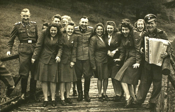 A group of female staff of Auschwitz with a few SS men laughing on a little bridge. One of the SS men holds an accordion.