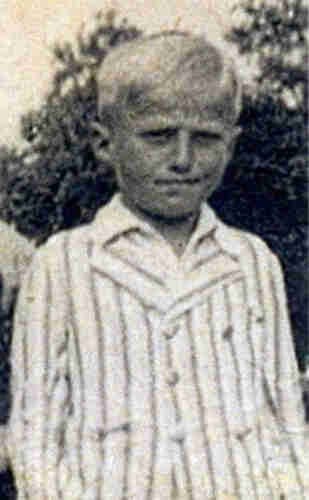 A boy photograhed outside. He is wearing a white jacket with dark stripes.
