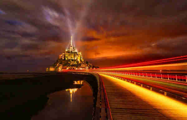 Abadía Mont Saint-Michell, Francia, iluminada por dos cañones de luz durante la noche.