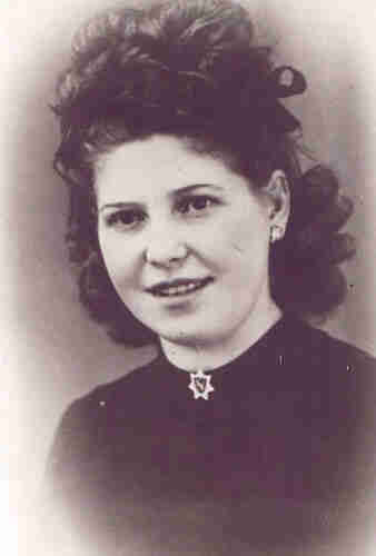 Black and white photo for ID. A young woman wearing a dark blouse with a star-shaped brooch under her neck. She has long curly hair pinned up. She has a slightly open mouth that exposes her upper teeth. 