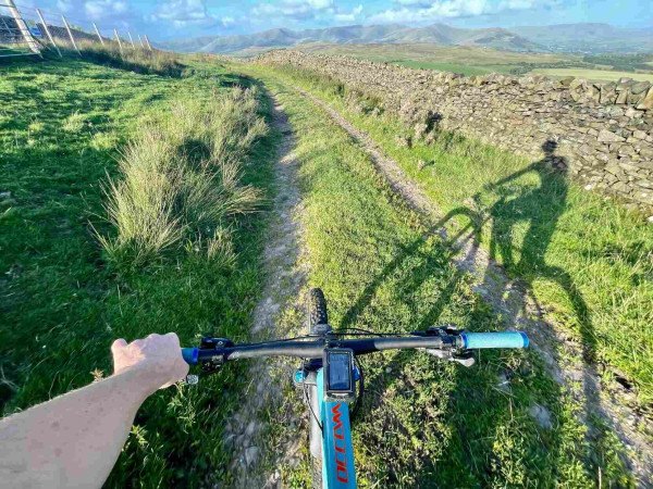 View down a double gravel track from a mountain bike with a cyclists shadow being cast 