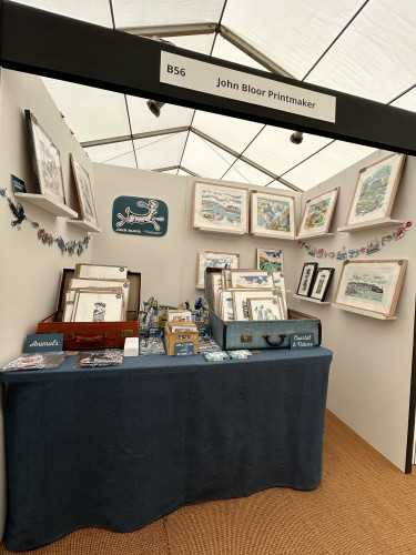 A photo of our stand at Craft Festival Bovey with various framed prints on the walls and print browsers made out of suitcases.