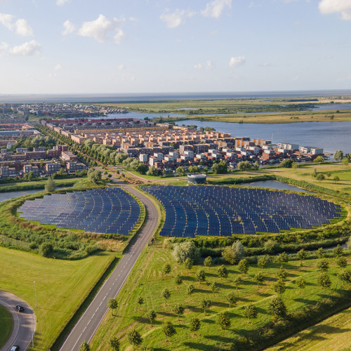 A round solar panel field, encircled by a road that leads to a residential area in Almere, the Netherlands. There are canals on both sides of the field. 