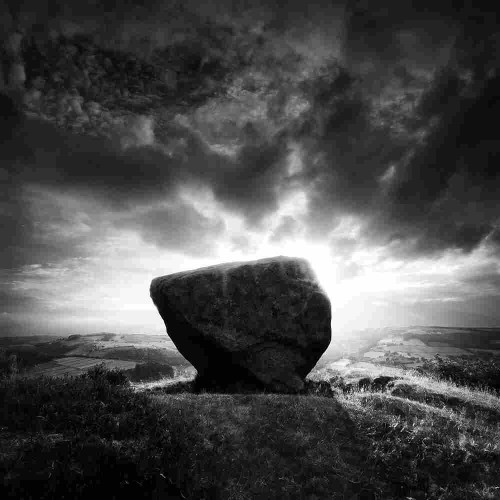 Atmospheric black and white photo of a glacially deposited rock, with dramatic sky.