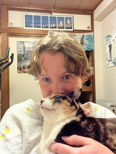 A selfie of me cuddling a calico cat. Her face is lifted to press up against my nose. 
