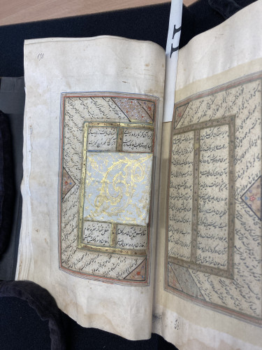 Open double facing page of a manuscript in Arabic, with black writing surrounded by gold and red borders, with flower decorations.