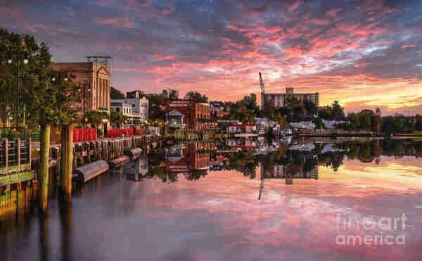 The Riverwalk at Wilmington, North Carolina is a charming and historic boardwalk along the Cape Fear River in downtown Wilmington, just in front of the Cotton Exchange. During our most recent visit, the colors in the sky were incredibly beautiful as they reflected in the waterfront. This scenic pathway, located along Water Street, offers breathtaking views of the river, complemented by the architectural beauty of historic buildings lining its route. From the Fine Art Gallery of Shelia Hunt.