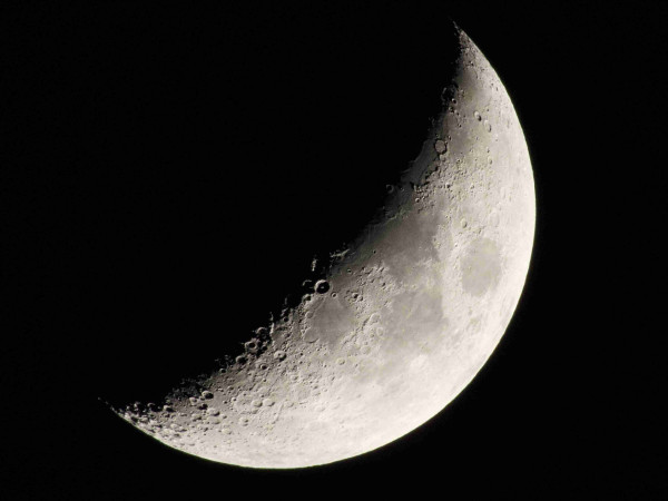A quarter moon, just about: a thick crescent moon with the craters at the terminus sharply delineated. The sky looks black but it’s an artefact of exposure, it was blue in reality.