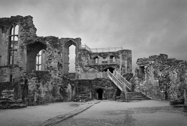 Black and white photo showing massive stone walls from inside the Castle. The walls seem almost to be stepped from lower to the right and higher to the left, where tall stone windows can be seen. A wooden structure of steps near the centre allows visitors to climb to the top of the middle wall.