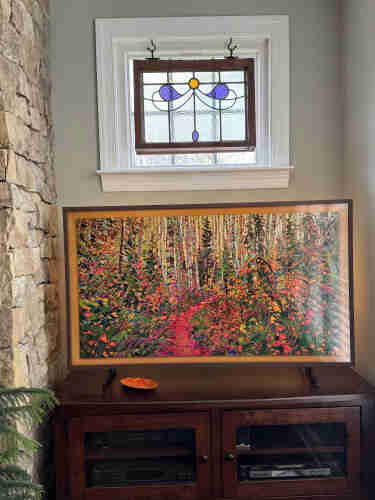 A snapshot of a corner of a family room.  The Frame TV sitting on furniture displays a bright, colorful image from the artist Erin Hanson, titled "Aspen Forest."

Above the TV there is a small, fixed window with an old piece of pebbly stained glass hanging in front of it, mostly clear with just a couple of comma-shaped pieces in purple and a round one in orange.  In a previous house we had collected many stained glass windows, but this home doesn't have as many spots.