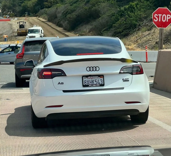A Tesla where the owner has removed the Tesla badges and put on Audi's logo, an "A5" badge, "2.0T", and an Audi license plate frame