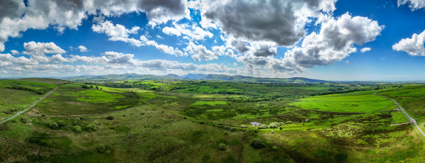 Panoramic shot taken by a drone over fields and farmland with distant mountains and cloud speckled skies above