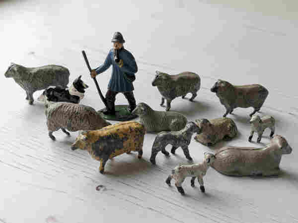 Colour photograph of a tableau of small lead farm animals, consisting of sheep, lambs, a sheepdog, and a shepherd.