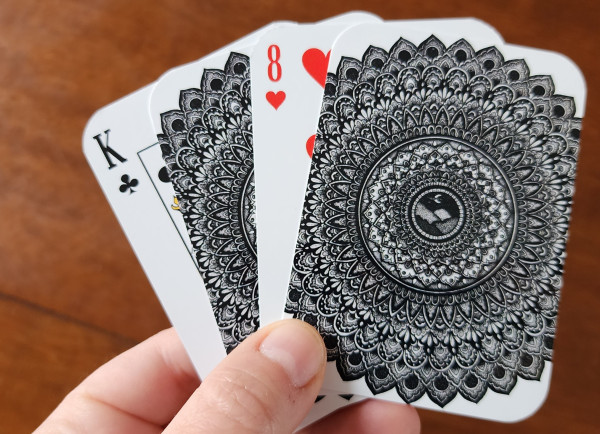 Holding up four playing cards, two facing number side up, two with the backs facing, an intricate mandala pattern printed on the back
